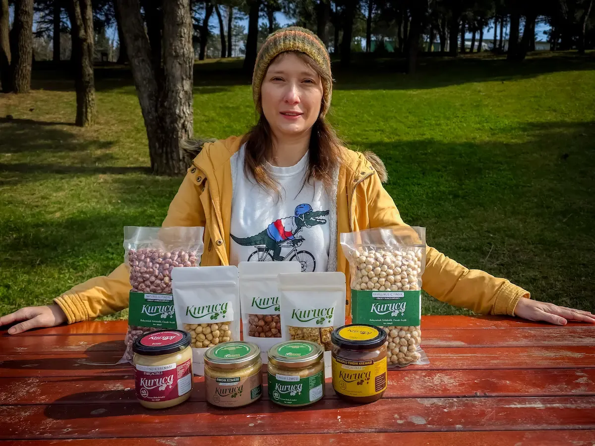 Dr. Yasemin Kuruca with Kuruca hazelnut products on a wooden table in a garden